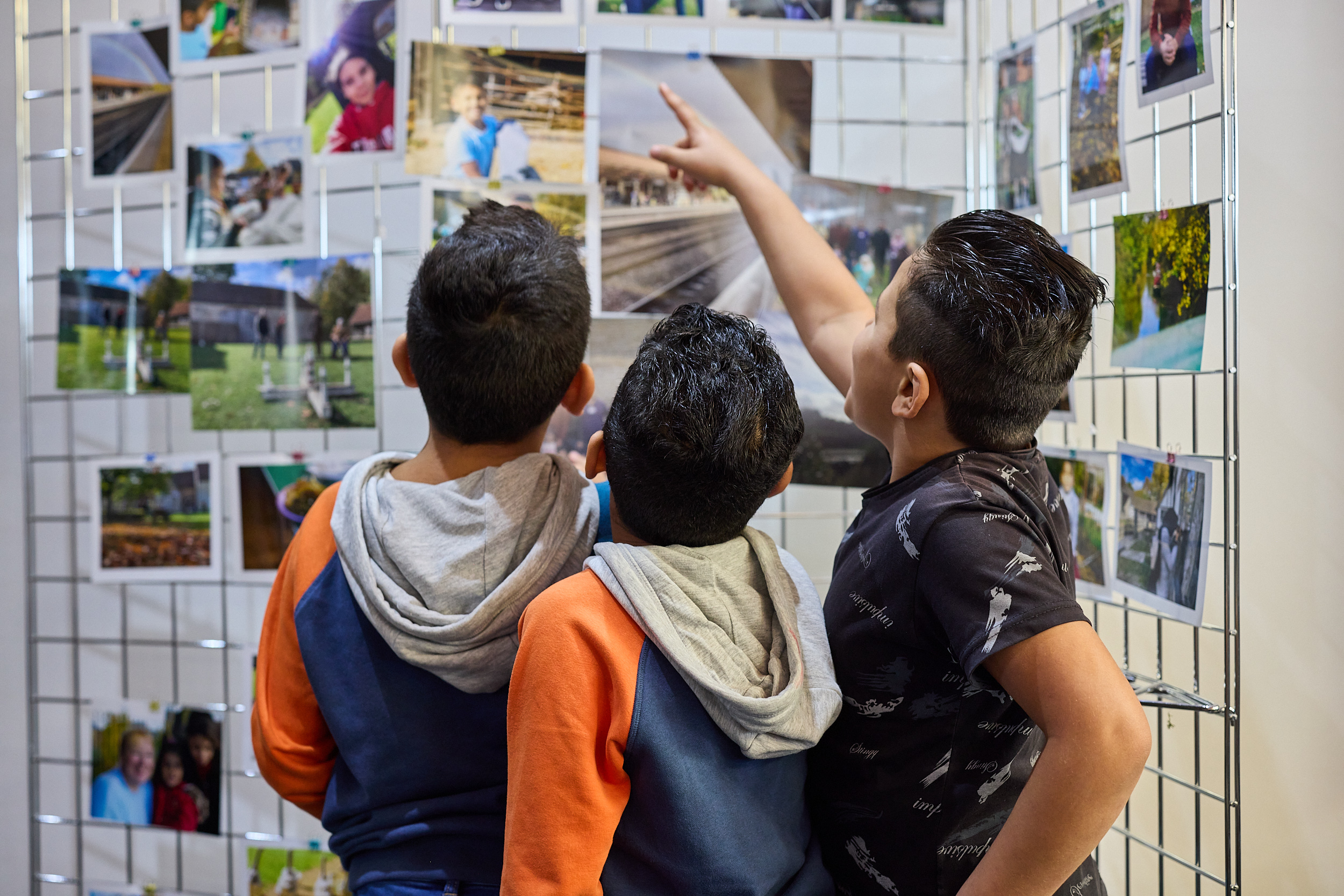 Three children are looking at a board of photos.