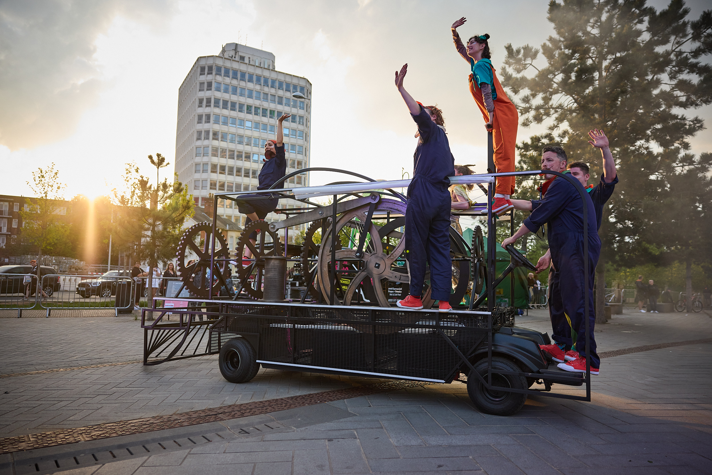 Performers balance on a golf cart turned into a train, waving at the crowds.