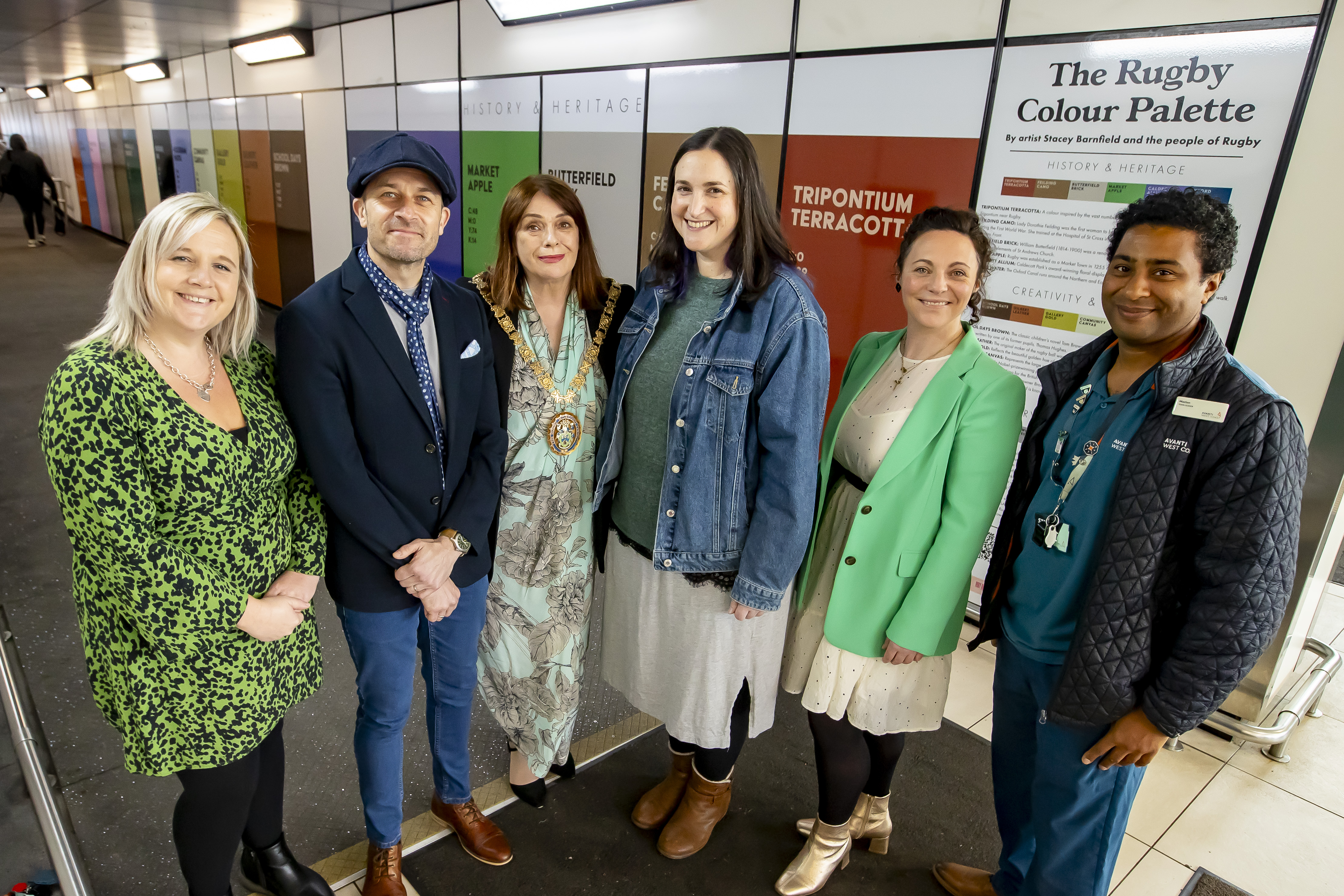 4 women and 2 men smile towards the camera in front of the Rugby Colour Palette at Rugby Station.